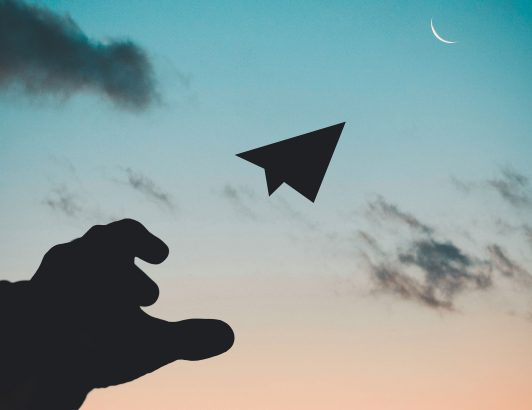 Silhouette of a hand reaching toward a cursor arrow pointing at a crescent moon in a pastel dusk sky with scattered clouds.