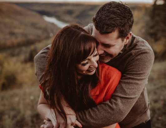 Couple embracing outdoors in natural landscape, sharing an intimate and affectionate moment during an autumn setting.