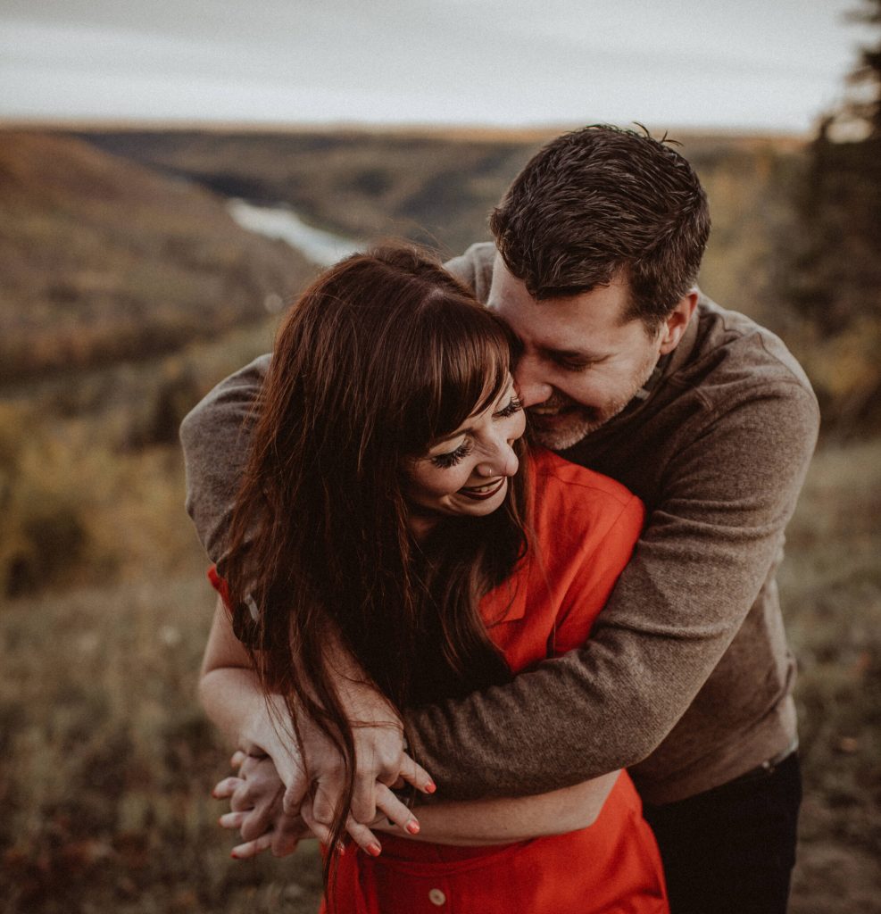 Couple embracing outdoors in natural landscape, sharing an intimate and affectionate moment during an autumn setting.
