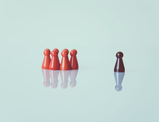 Red game pieces grouped together facing a single black piece on reflective surface, symbolizing individuality, isolation, or observing others.