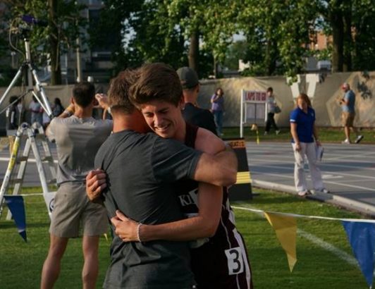 Two athletes hugging on outdoor track field after race, celebrating achievement and sportsmanship at athletic event.