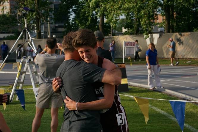 Two athletes hugging on outdoor track field after race, celebrating achievement and sportsmanship at athletic event.