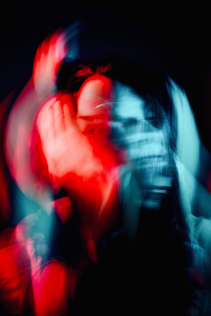 Abstract portrait with heavy motion blur showing a person’s face and hands streaked in red and blue light against a dark background, creating a sense of movement and intensity.