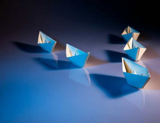 Small blue paper boats arranged on glossy surface with soft lighting, representing creativity, leadership, and minimalist design concept.