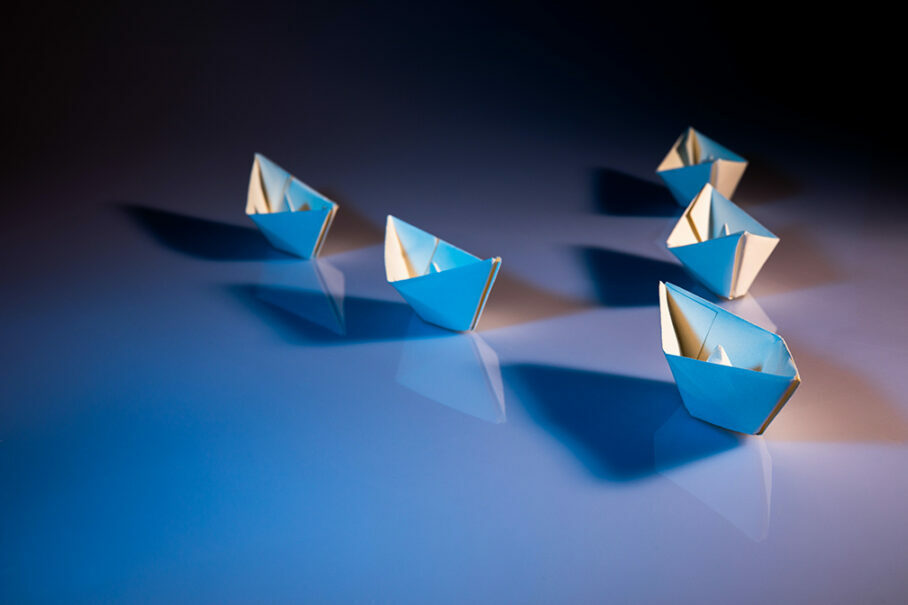 Small blue paper boats arranged on glossy surface with soft lighting, representing creativity, leadership, and minimalist design concept.