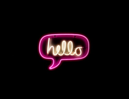 Pink neon speech bubble sign displaying the word hello against black background, symbolizing greeting, communication, and modern design.