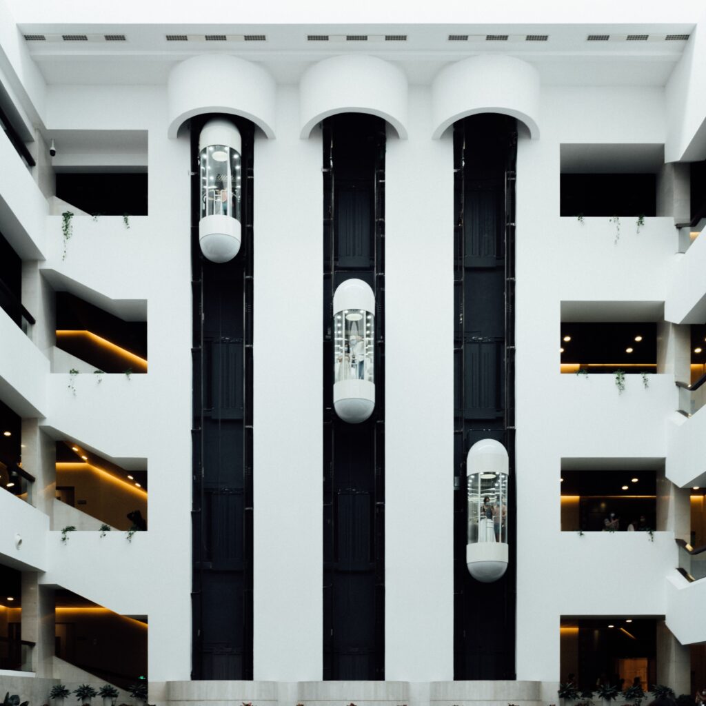 Modern building atrium with glass elevators and symmetrical white architecture, showcasing contemporary interior design and vertical transport.
