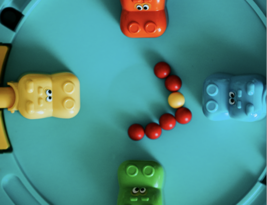 Colorful plastic hippo toys arranged around game board with marbles, representing a classic Hungry Hungry Hippos board game.